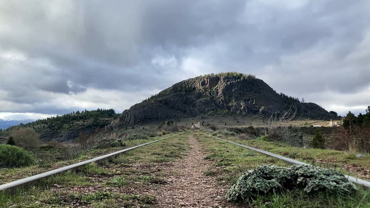 Vías de tren hacia una montaña, bajo un cielo nublado